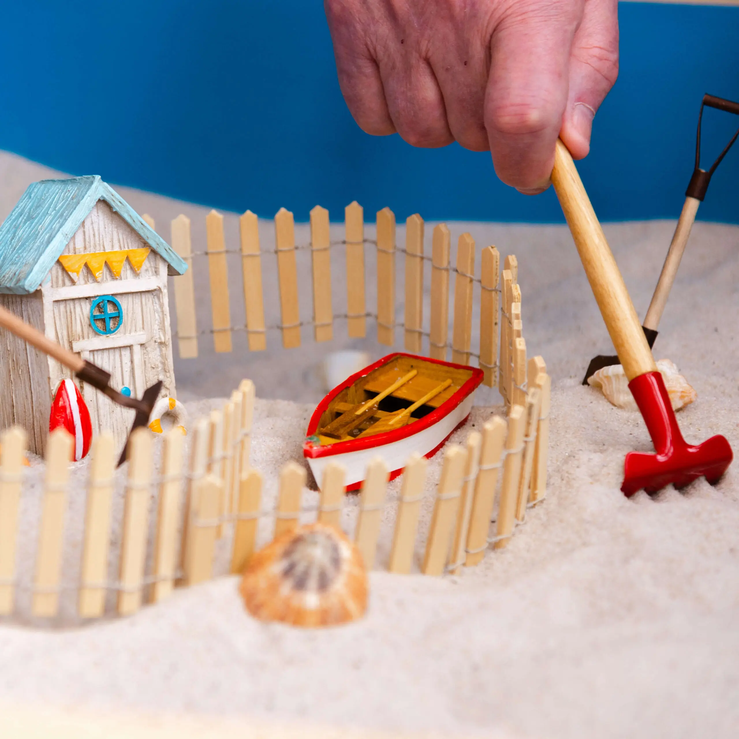 A hand arranging miniature objects in a sand tray